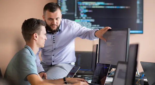 A mentor and mentee working together at a computer, collaborating on code